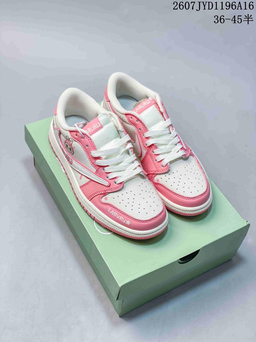 Pair of pink and white Jordan low-top sneakers displayed on a green shoebox, with Labubu graphics and white laces visible.