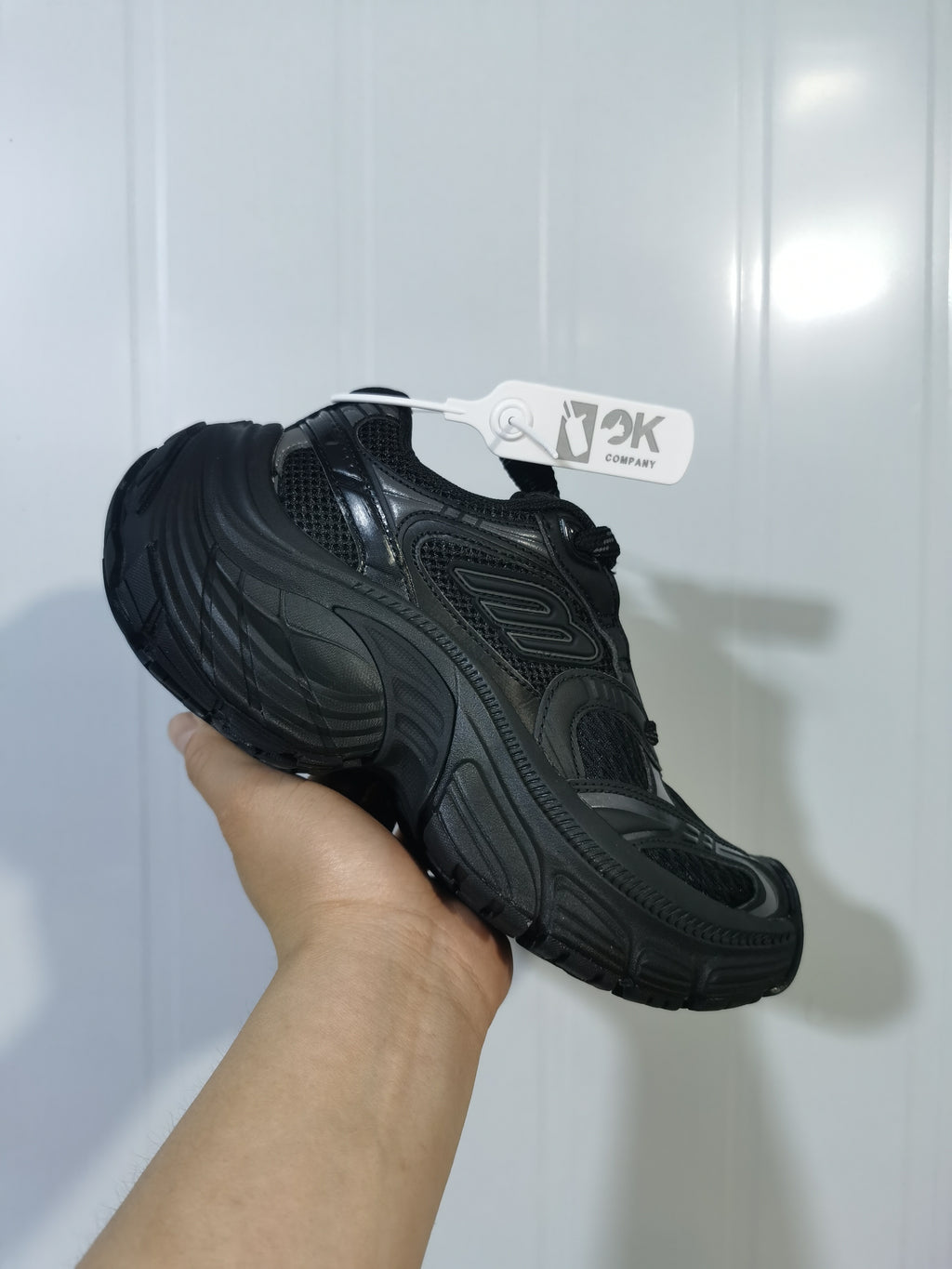 Angled side view of the black sneaker showing layered mesh panels, glossy overlays, and the thick sculpted outsole.