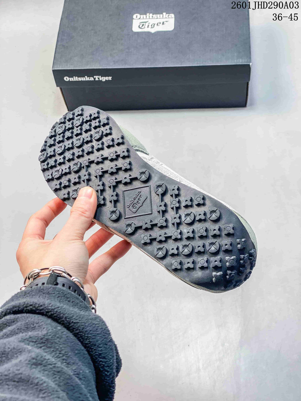 Close view of the patterned black outsole of an Onitsuka Tiger sneaker beside its branded box.
