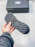 Close view of the patterned black outsole of an Onitsuka Tiger sneaker beside its branded box.