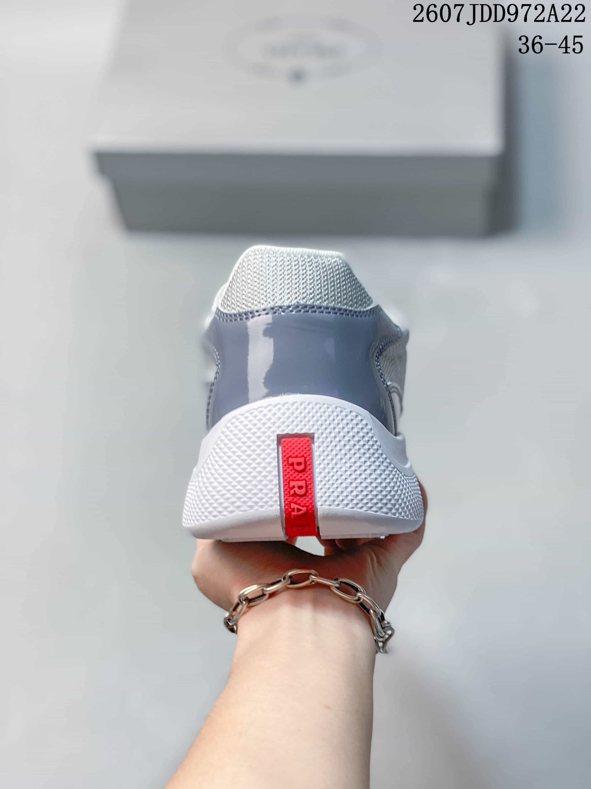 Rear view showing the white outsole, gray heel panel, and red Prada heel pull tab.