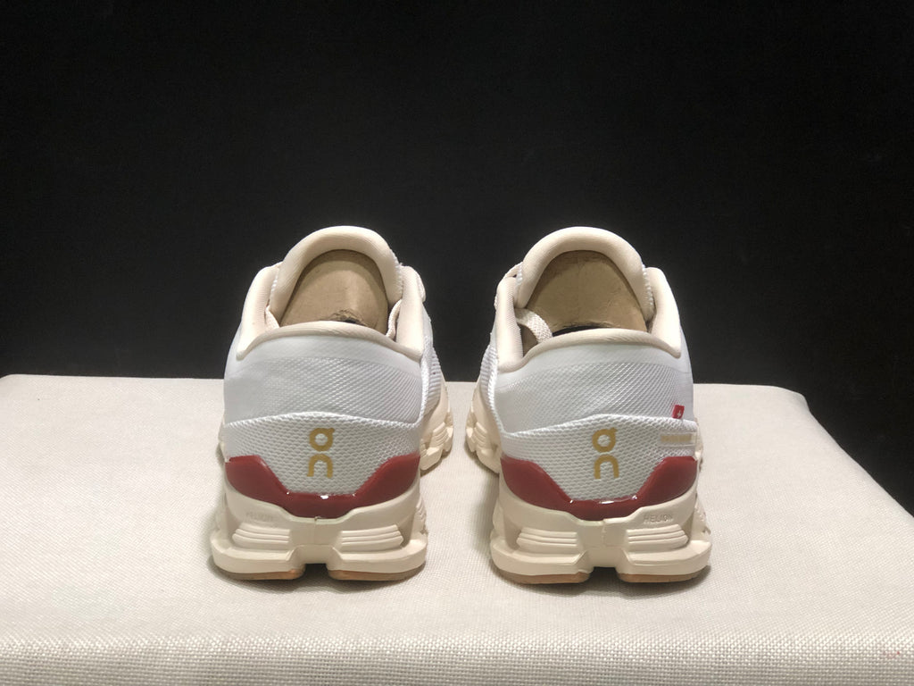 Rear view of the white On Cloud X4 pair showing gold heel branding and burgundy heel accents.