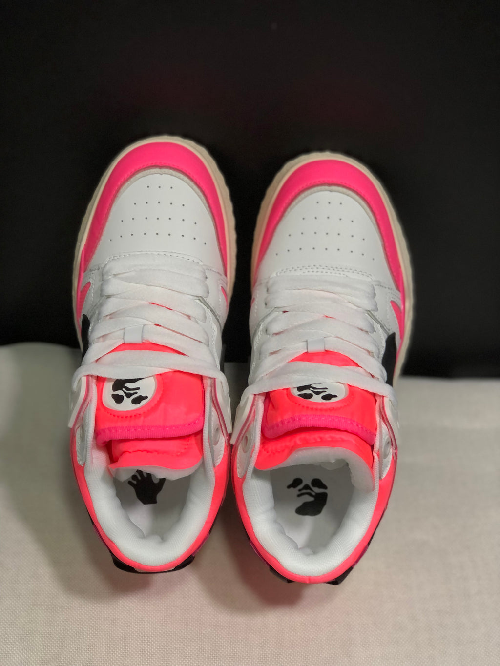 Top view showing white perforated toe panels, white laces, pink tongues, and printed tongue and insole details.