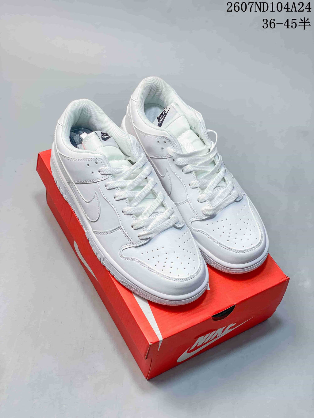 All-white Nike SB Dunk Low sneakers displayed on a red shoebox.