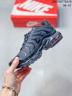 Side view of a black Nike Air Max Plus sneaker highlighting the layered upper, wavy overlays, side branding, and midsole cushioning.