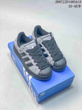 Gray and black adidas shell-toe sneakers displayed on a blue shoebox.