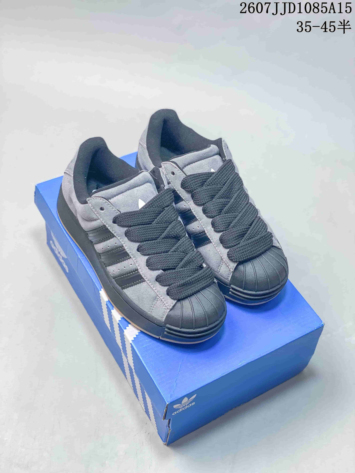 Gray and black adidas shell-toe sneakers displayed on a blue shoebox.