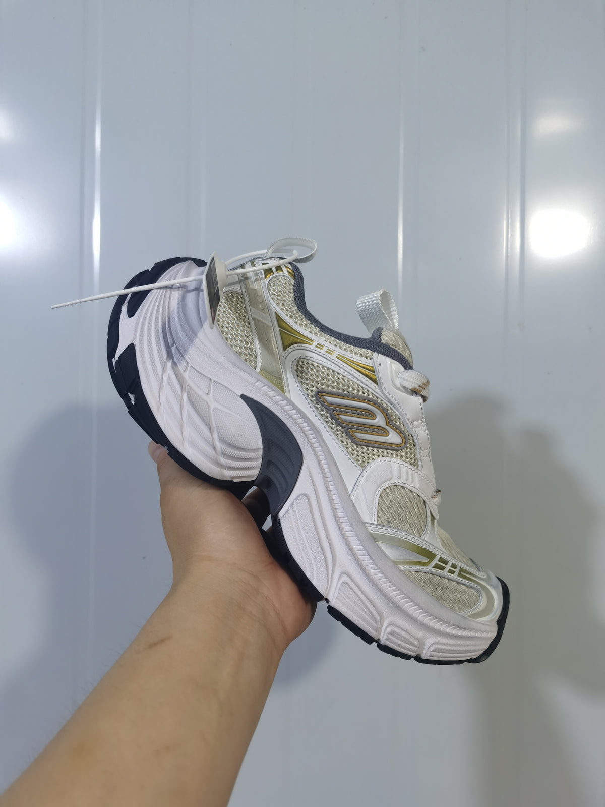 Side view of beige, gold, white, gray, and black Skechers sneakers with layered panels, mesh sections, and a sculpted white sole.
