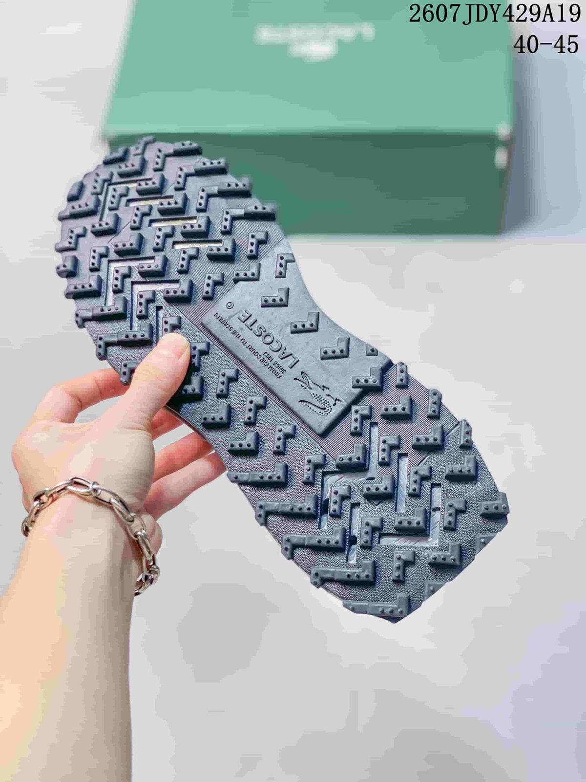 Close view of the sneaker outsole showing a raised, geometric tread pattern and Lacoste branding.