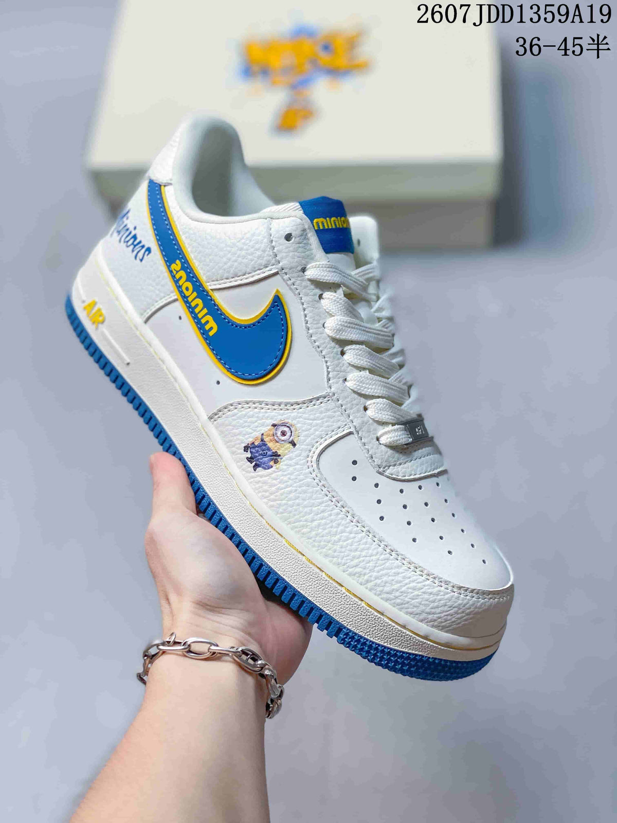 Close-up of a white low-top sneaker with a blue-and-yellow Swoosh, white laces, blue outsole, and small character artwork; image text shows style code 2607JDD1359A19 and size range 36-45.