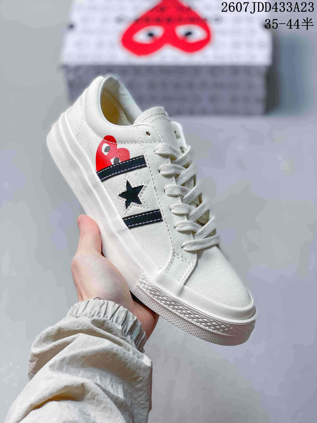 Close-up of a white low-top sneaker showing the dark side stripes, star emblem, heart-eye graphic and textured rubber outsole.