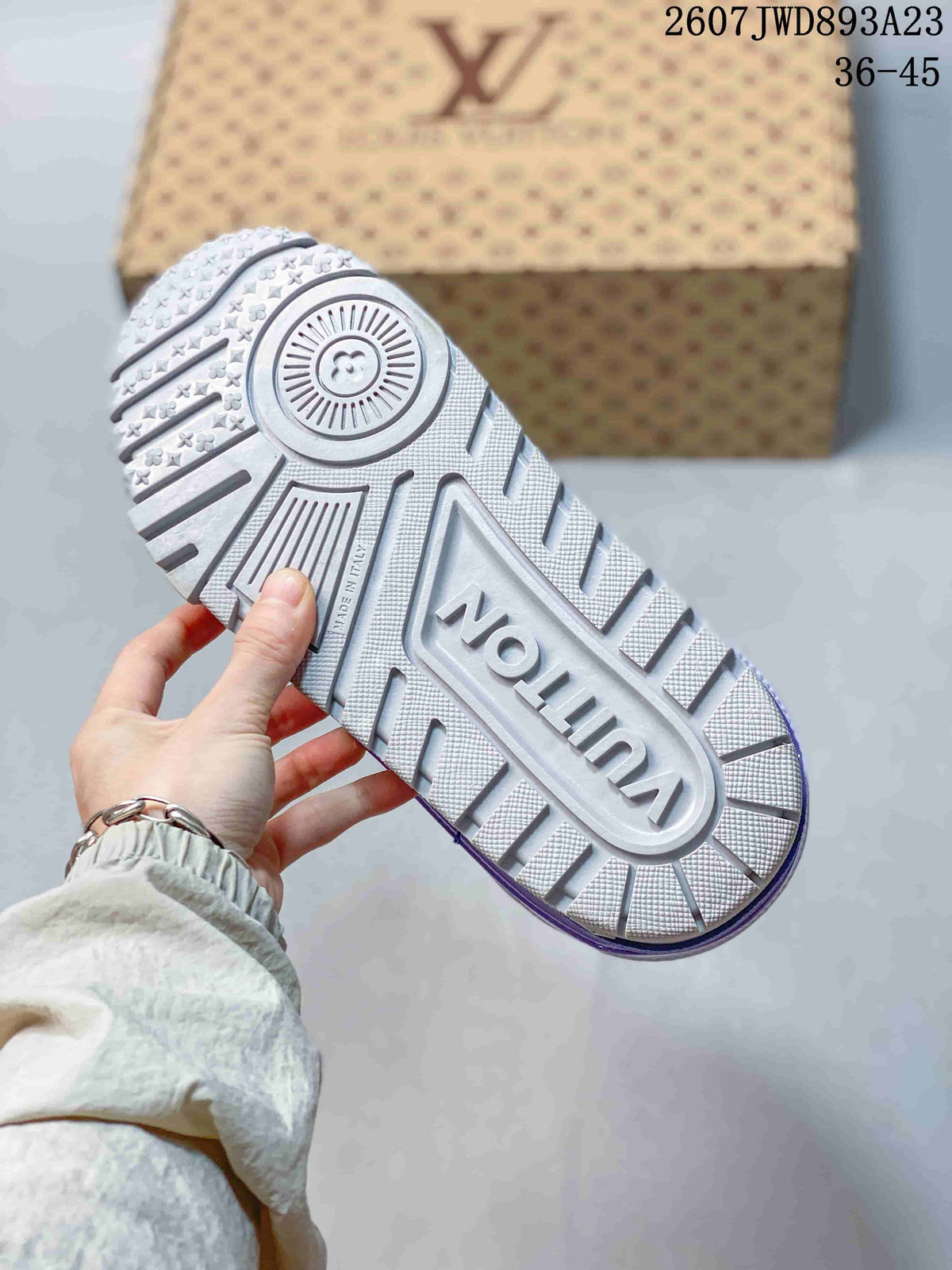 Bottom view of the sneaker showing the white and purple outsole with geometric tread, embossed branding, and patterned heel detail.