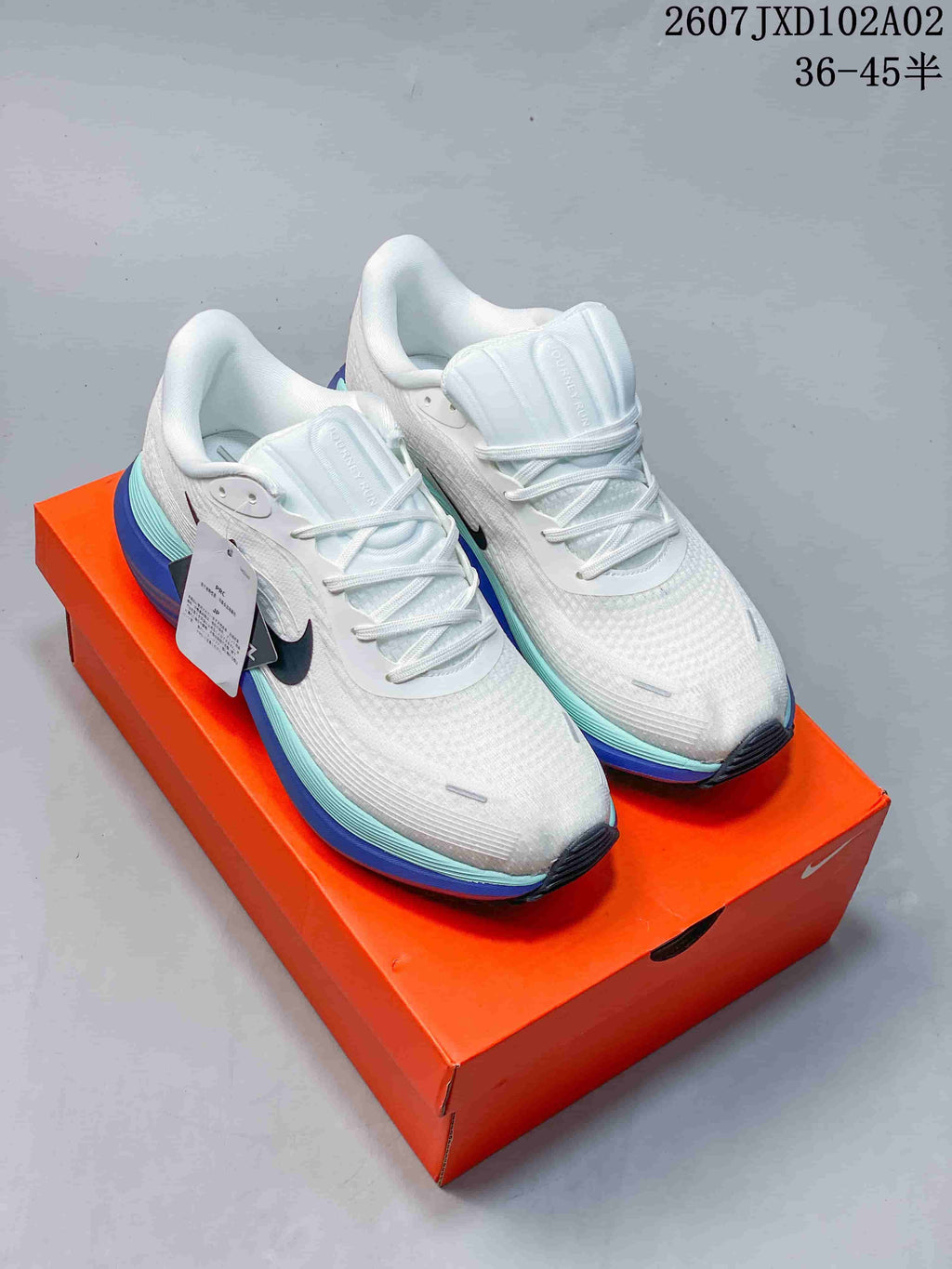 Pair of white Nike Vomero running shoes with aqua and blue midsole accents on an orange box