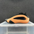 Side view of an orange and black low-top sneaker with a sculpted panel and sole.