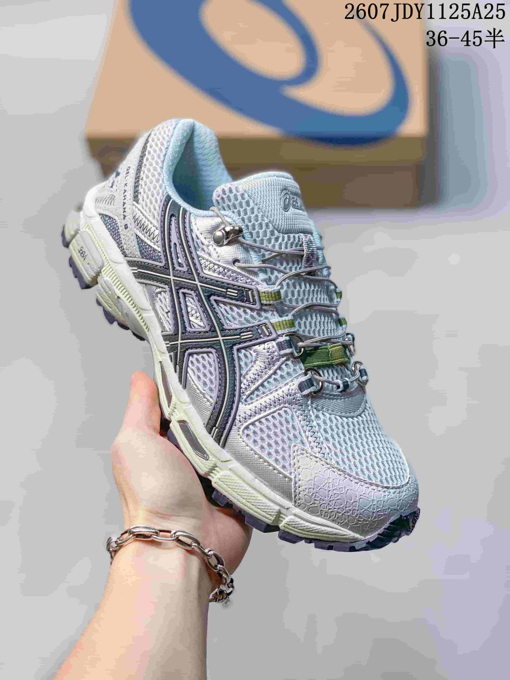 Angled side view of the ASICS sneaker showing the light grey upper, dark side detailing, green accents, and rugged outsole; image text shows style code 1125A25 and size range 36–45.