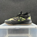 Side view of low-top sneakers with green, tan, and black camouflage panels, a black collar and sole, and a gum-colored outsole.