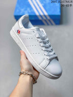 Close side view of a white adidas Stan Smith sneaker with a navy heel accent, perforated upper, and white rubber-style sole.