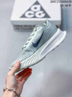 Side view of the pale green Nike ACG sneaker showing the navy Swoosh, textured upper, lace area, and white midsole.