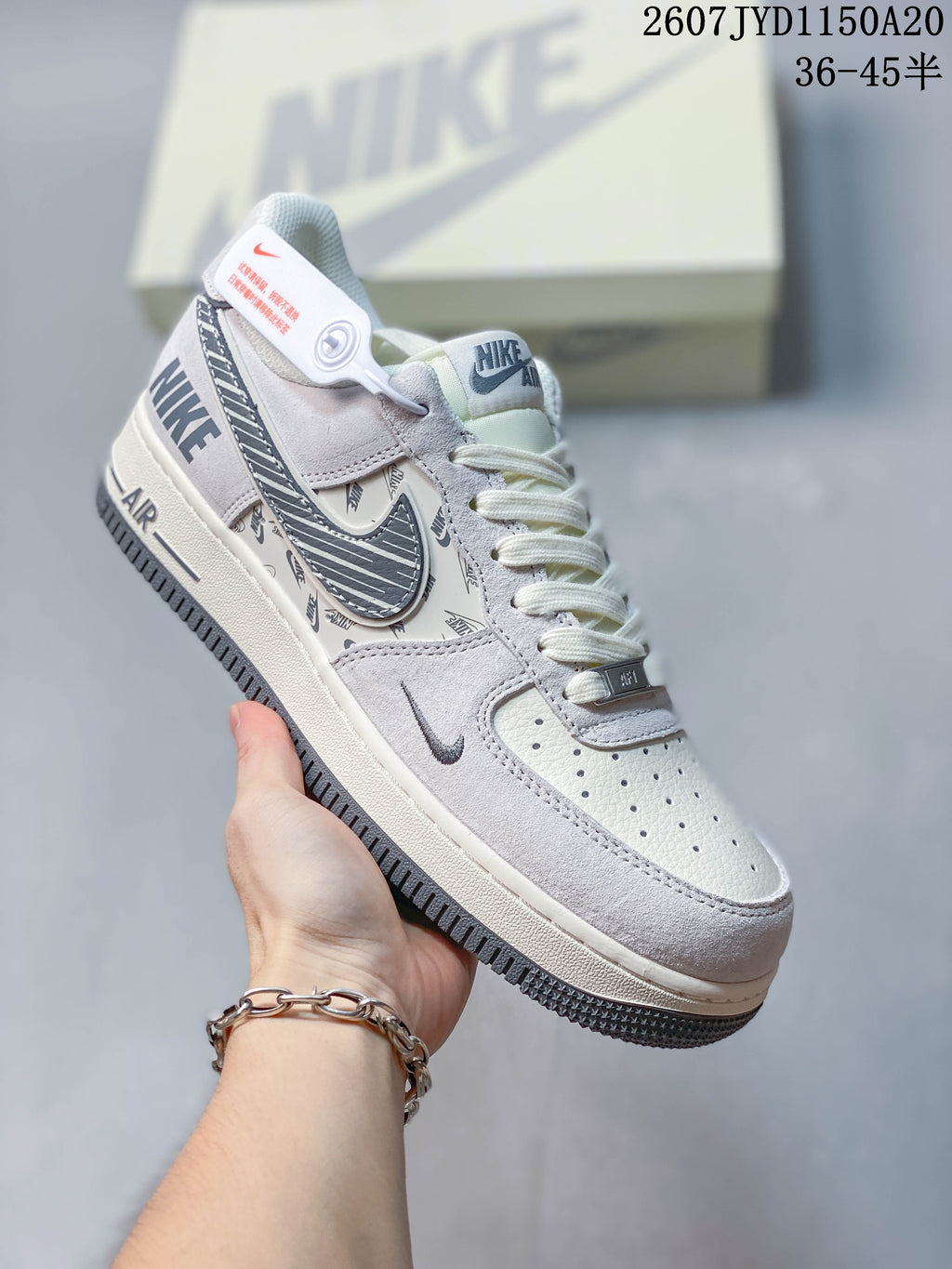 Angled side view of the white and gray Nike sneaker showing the Air Force 1-style midsole, patterned Swoosh, heel branding, and attached tag.