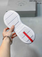 Underside view of a white sneaker showing the textured outsole, central branding detail, and red heel strip.