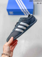 Side profile of a dark gray low-top sneaker showing white side stripes, lace-up construction and a flat rubber outsole.