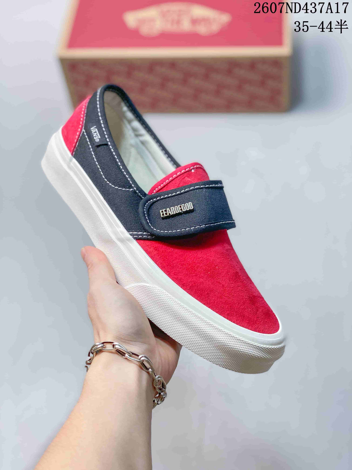 Side view of a red and navy Vans slip-on sneaker showing the strap, suede-textured upper, Vans branding, and white rubber sole.