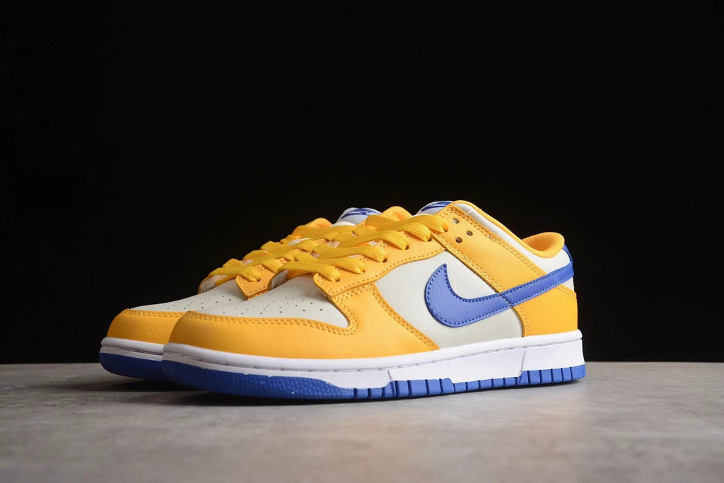 Angled front-side view of the pair highlighting the wheat gold overlays, light-colored toe boxes, and blue Swooshes.