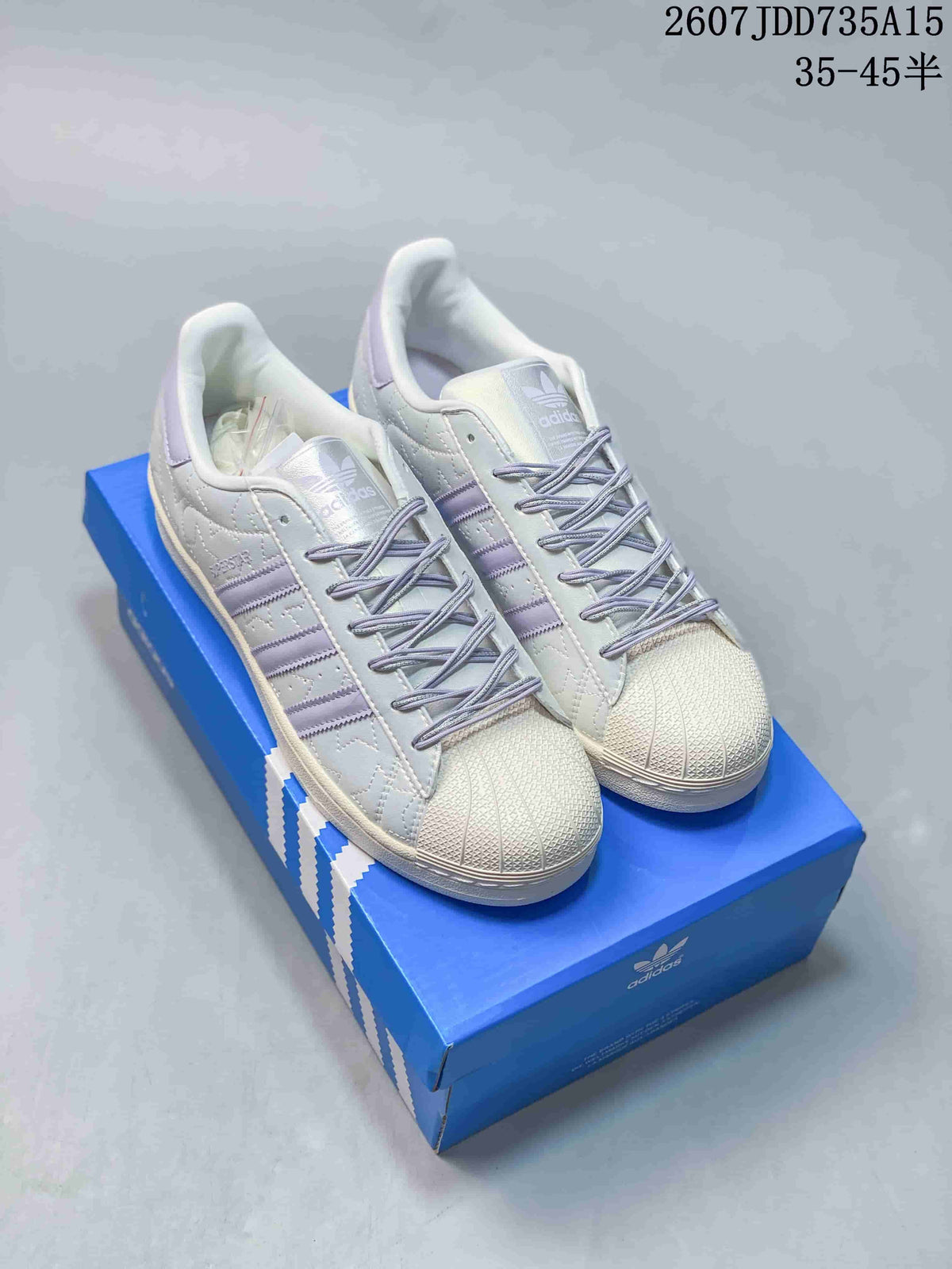 Pair of white and lavender adidas Superstar sneakers displayed on a blue shoebox.