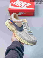 Angled side view of the Nike Zoom Vomero 5 sneaker showing white and cream panels, navy Swoosh, and orange accent detailing.