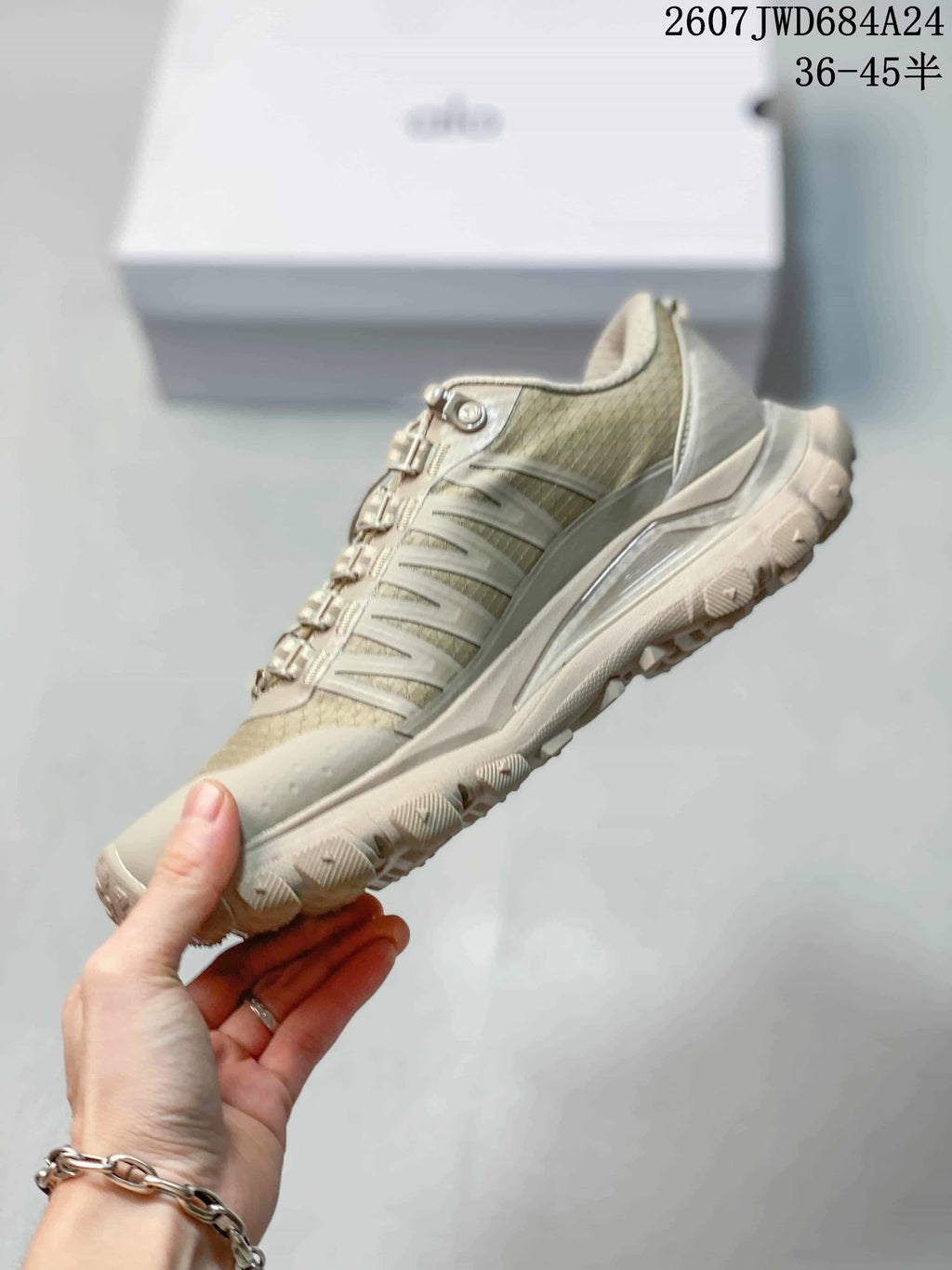 Side view of the beige-toned sneaker showing its layered upper, structured sole, and lugged outsole.