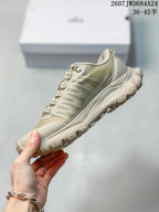 Side view of the beige-toned sneaker showing its layered upper, structured sole, and lugged outsole.