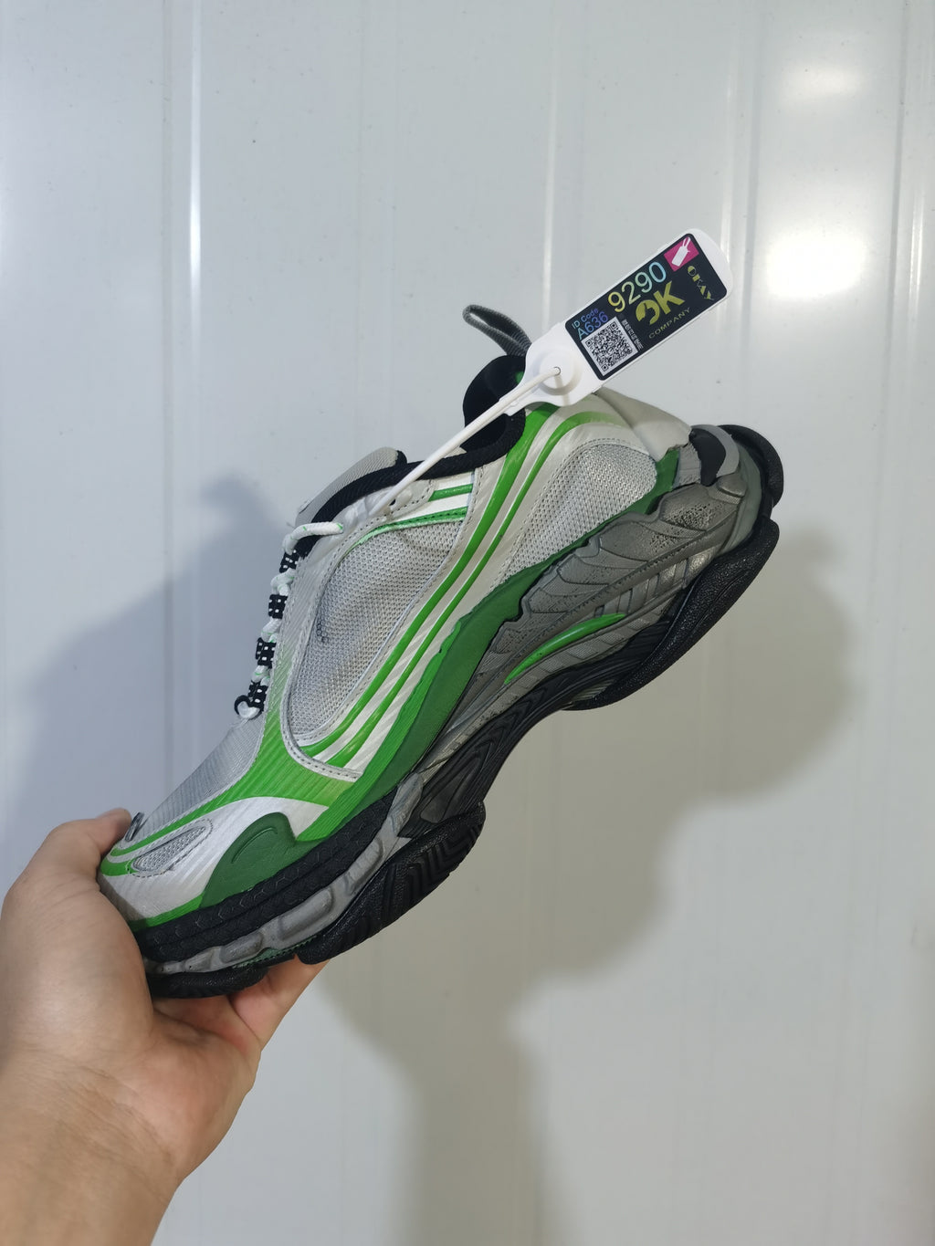 Angled view of the grey and green sneaker highlighting the layered upper, green accents, black outsole, and attached product tag.
