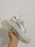 White Balenciaga sneaker held at an angle, showing the layered upper, side branding, and translucent sole.