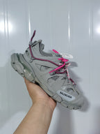Angled view showing the grey layered upper, mesh-style panels, pink laces and chunky outsole of the sneaker.