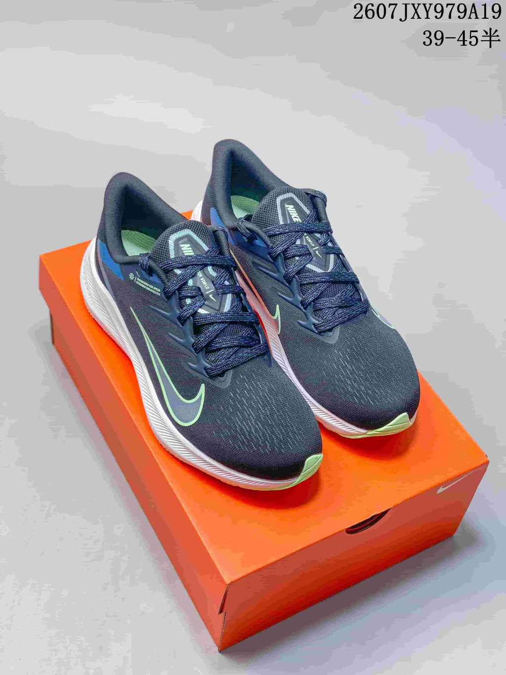 Pair of dark navy and black Nike running sneakers with blue and green accents displayed on an orange shoebox; overlay shows style code 2607JXY979A19 and size range 39–45.