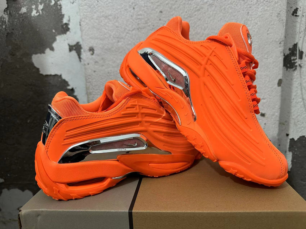 Pair of bright orange sneakers shown from the side, highlighting their sculpted design and silver-tone accents.