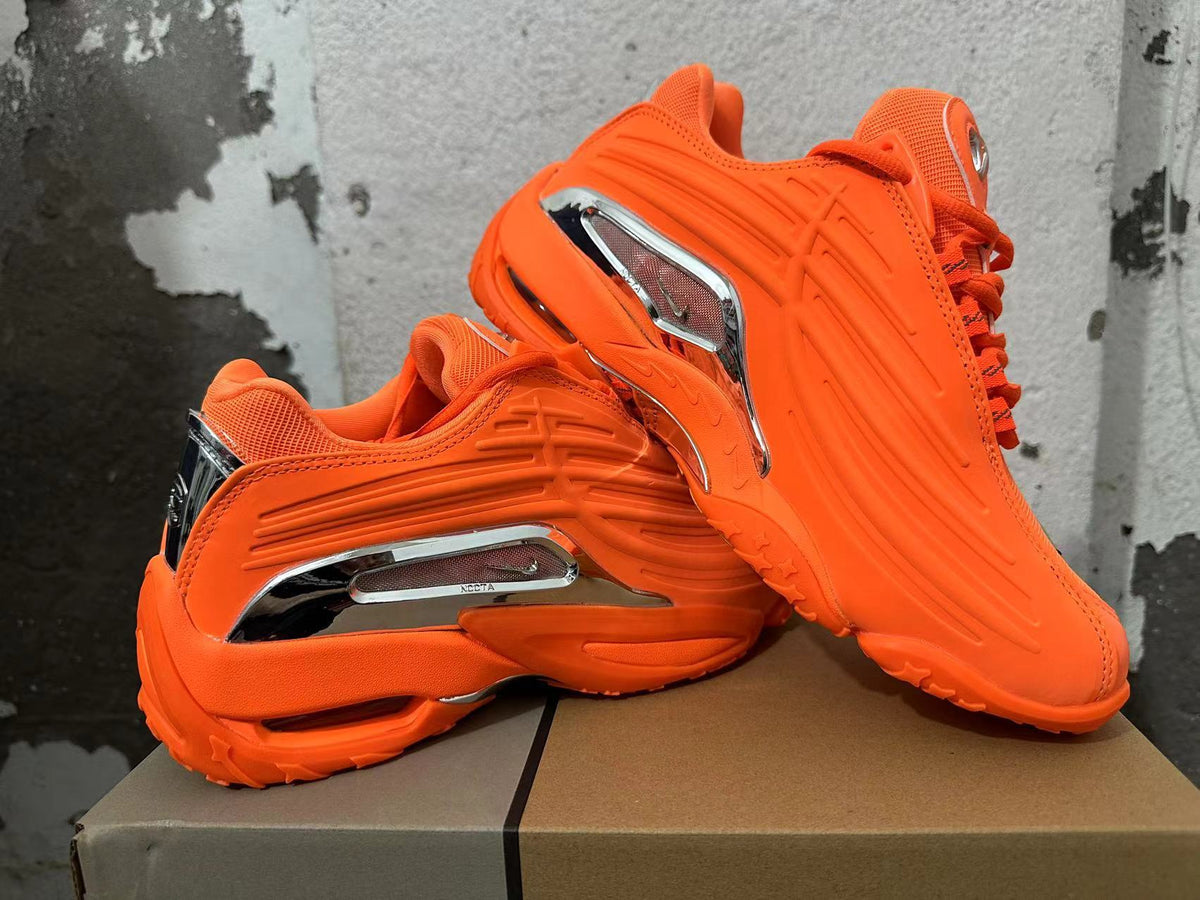 Pair of bright orange sneakers shown from the side, highlighting their sculpted design and silver-tone accents.