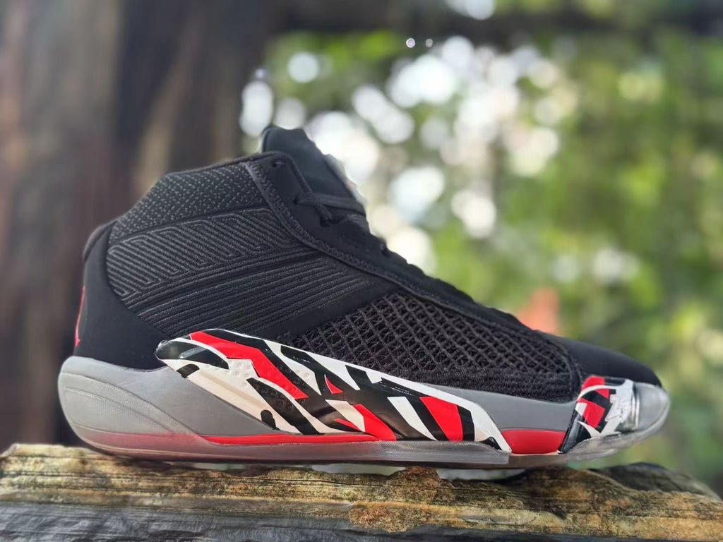 Side view of a black Jordan XXXVIII shoe with red, white, and gray graphic accents