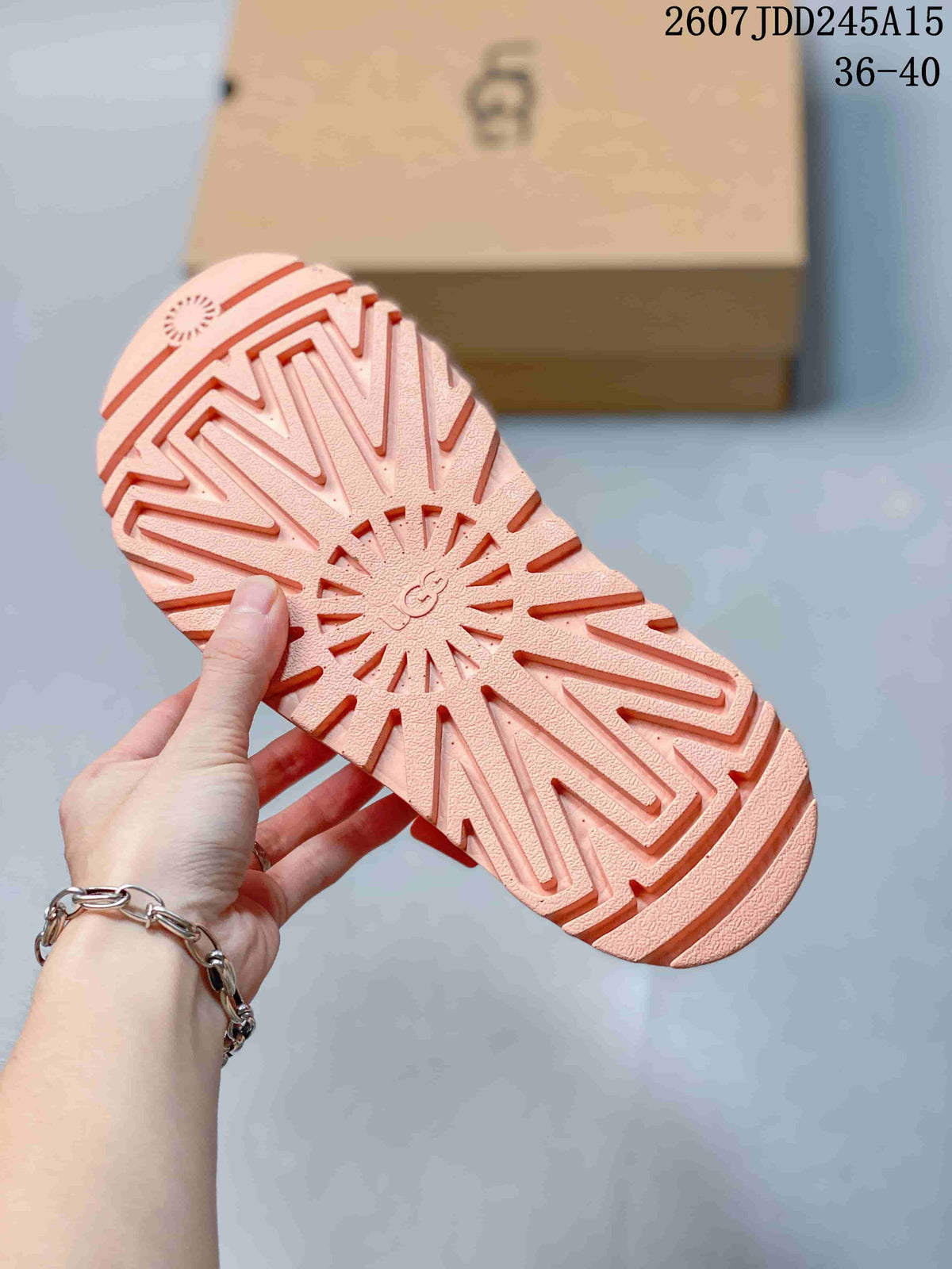 Underside of the pink sandal showing the raised lug-pattern outsole and central UGG branding.