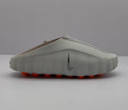 Side view of a gray Nike slide sandal showing the textured upper, sculpted sole, and orange outsole elements.