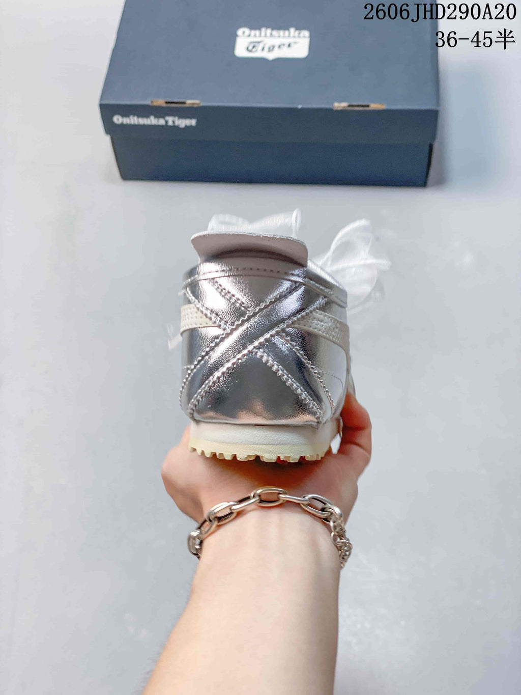 Rear view of a silver sneaker showing crossed heel panels and cream outsole.