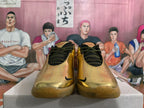 Front view of gold-tone Nike sneakers showing black patterned laces and translucent gum-colored outsoles.