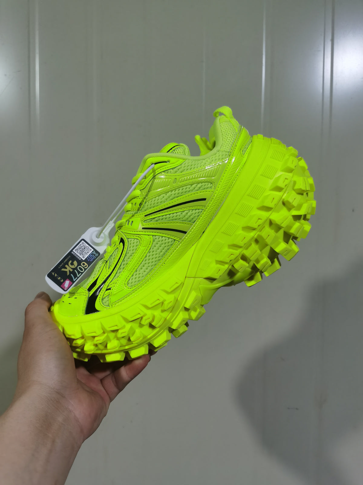 Bright green chunky sneaker held in hand, showing the layered upper, black accent lines, lace-up front, and deep lugged outsole.