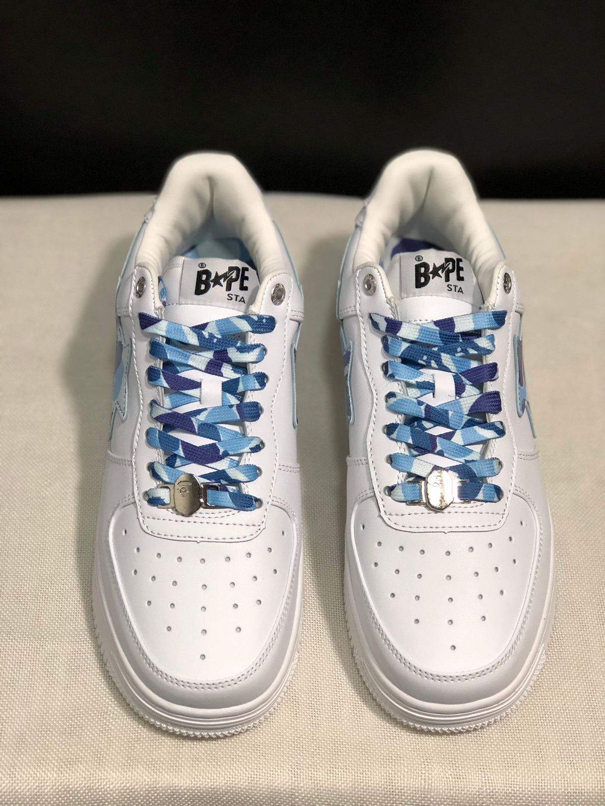 Front top view of the pair showing the perforated white toe panels and blue patterned laces with metal accessories.