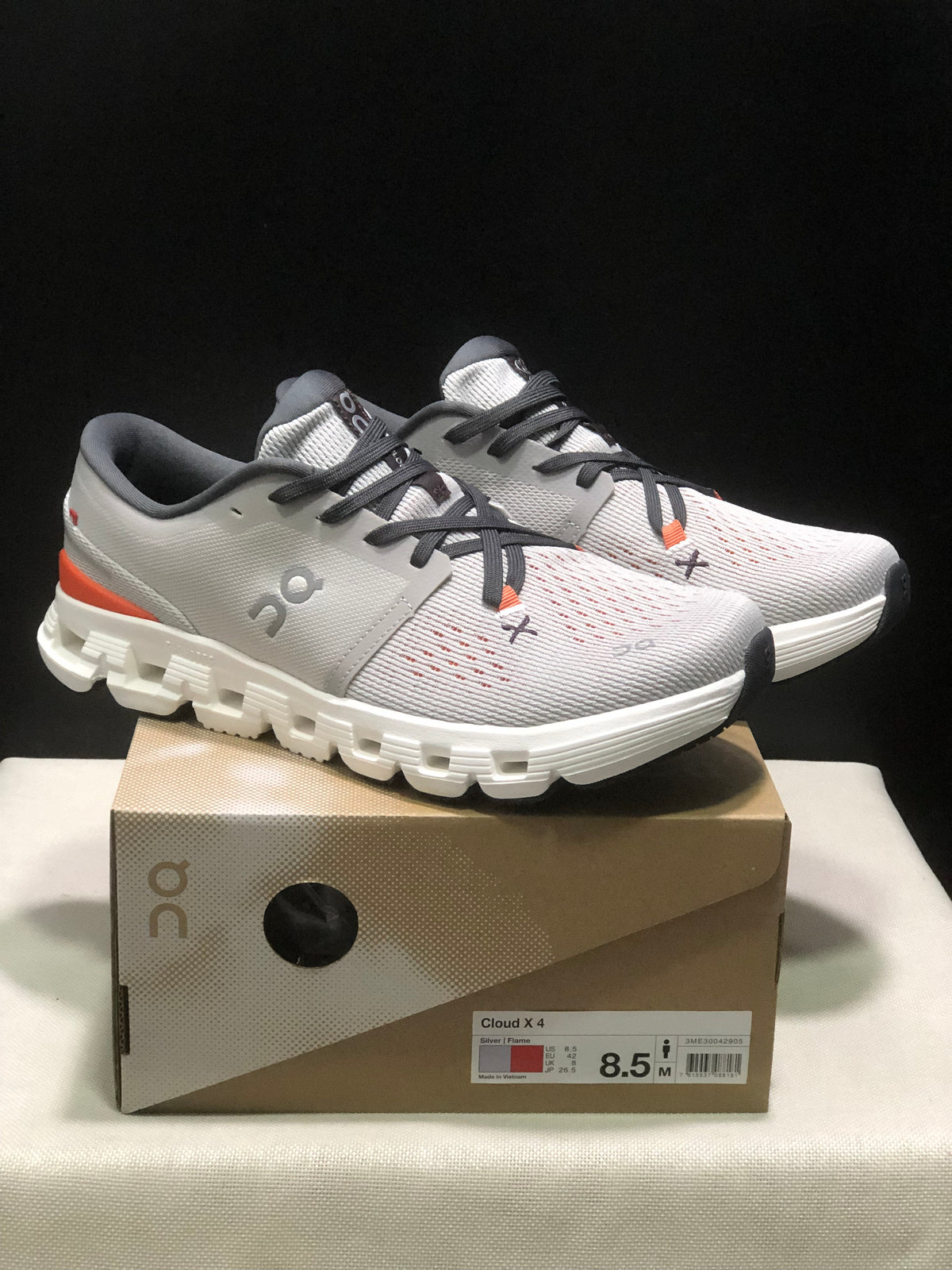 Pair of silver and flame On Cloud X4 shoes displayed on their product box, with the box label visible.