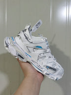 Close angled view of the white sneaker showing mesh sections, black graphic lines, blue accents, and lace-up construction.