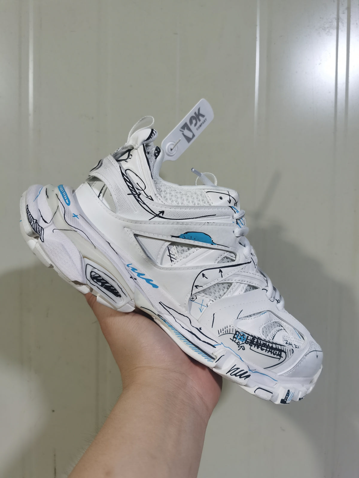 Close angled view of the white sneaker showing mesh sections, black graphic lines, blue accents, and lace-up construction.