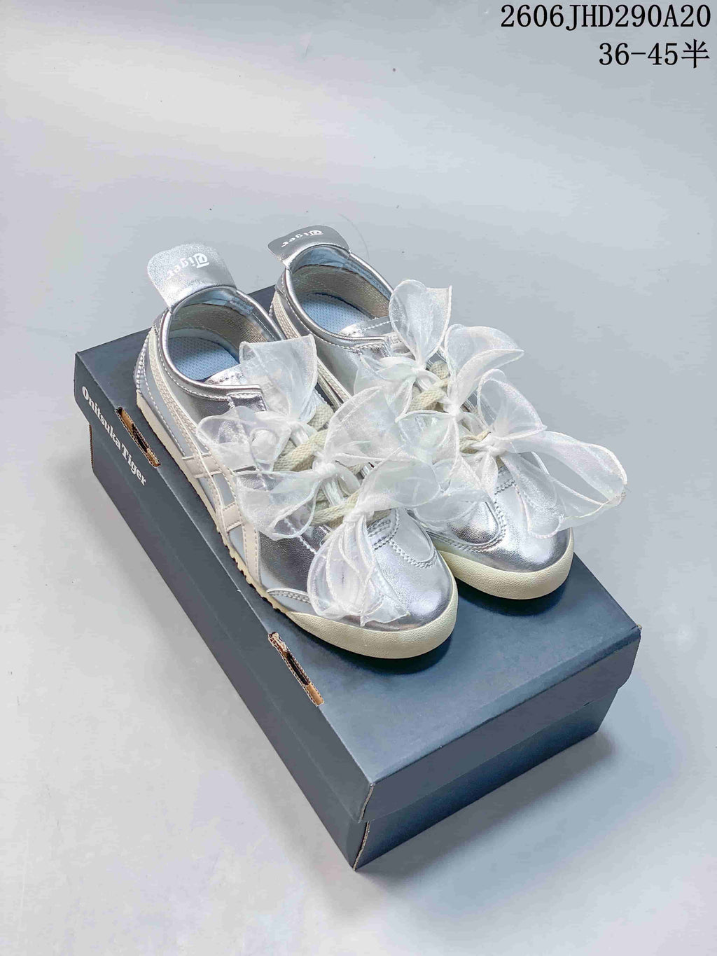 Pair of silver Onitsuka Tiger-style sneakers with sheer bow laces on a shoebox; image overlay shows a size range.