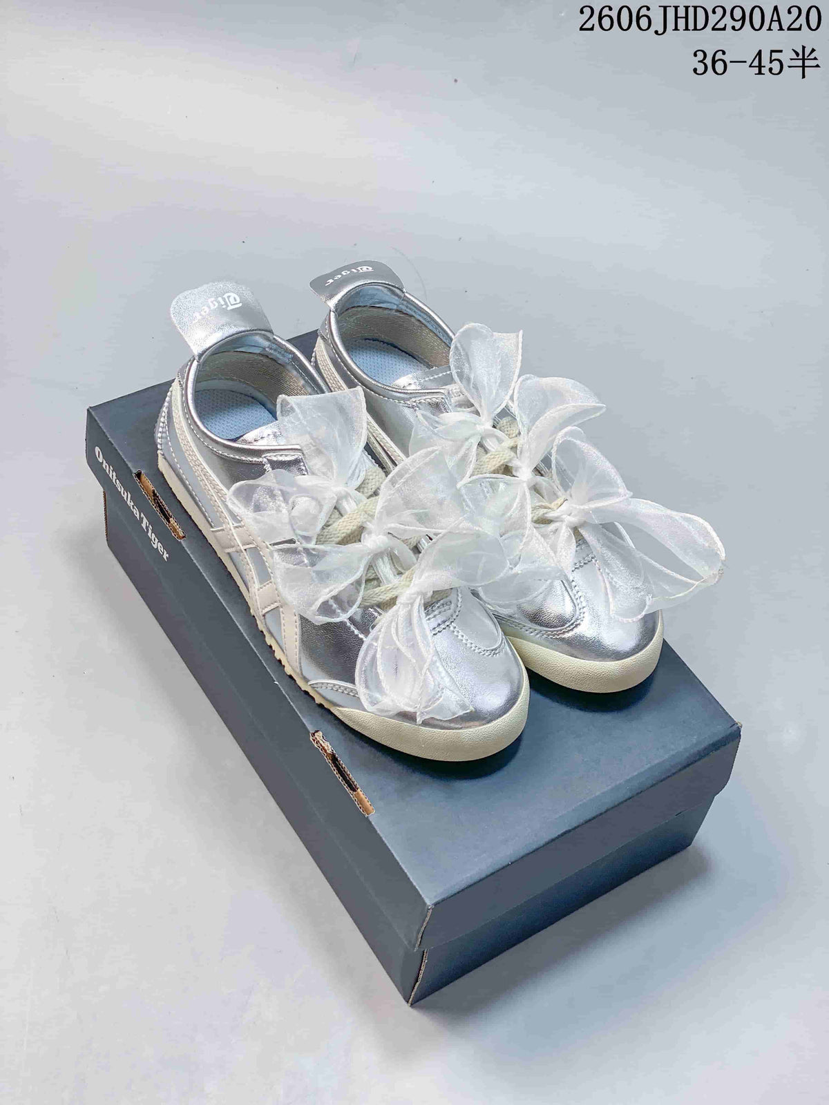 Pair of silver Onitsuka Tiger-style sneakers with sheer bow laces on a shoebox; image overlay shows a size range.