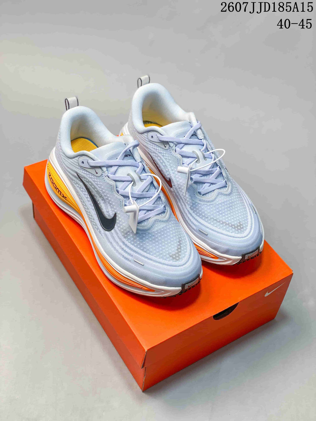 Light blue-white Nike Vomero Plus sneakers displayed on an orange shoebox.